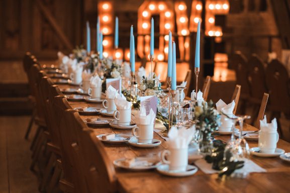 Festlich gedeckter Hochzeitstisch mit Kerzen, Blumen und Geschirr, im Hintergrund leuchtende „LOVE“-Buchstaben.