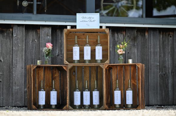 Rustikale Sitzordnung mit beschrifteten Flaschen in Holzkisten, dekoriert mit Blumen.
