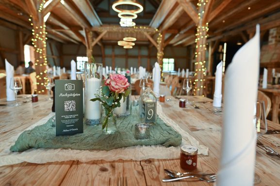 Hochzeitstisch in rustikaler Scheune mit Kerzen, rosa Rose, Tischnummer 9 und QR-Code-Schild für Fotos.
